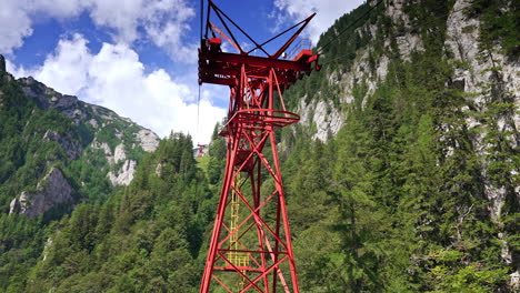cable car tower by mountains. a red cable car tower rises above a lush green forest, surrounded by towering mountains and vibrant blue skies