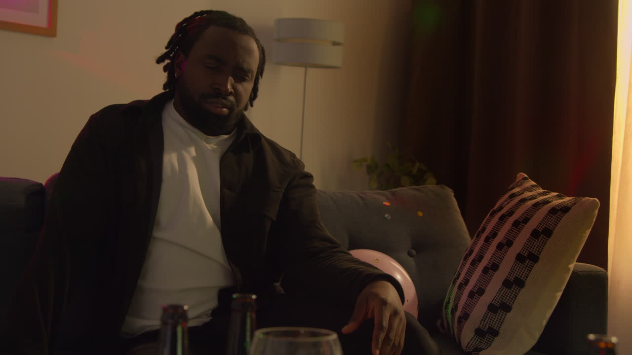 Man Sitting On Sofa Recovering From Drinking Alcohol At House Party Suffering With Hangover