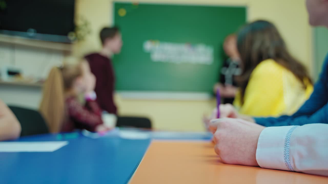 Blurred classroom background. Students sitting in class and teacher talking to a teen school child near the blackboard at school. Education concept.