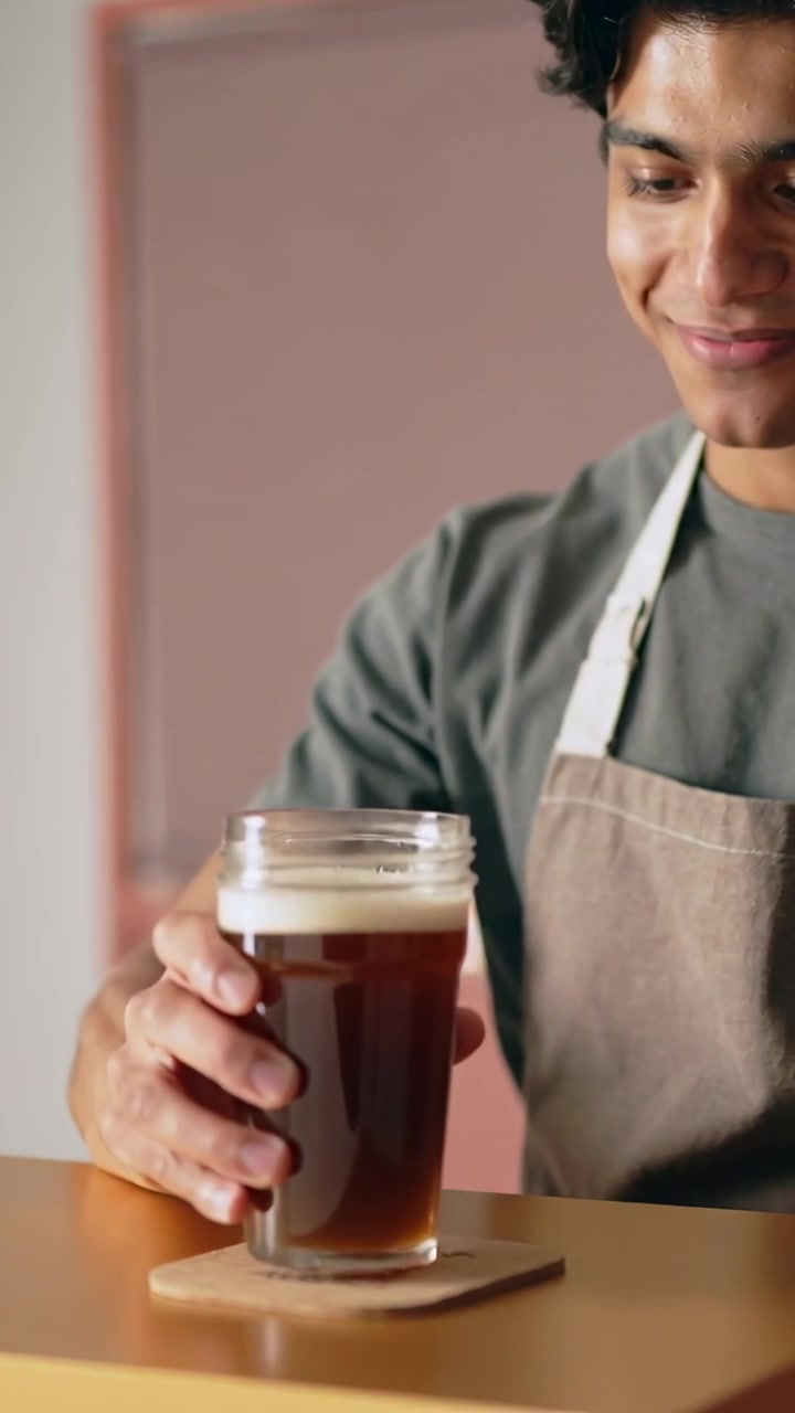 Vertical video: Lifting barista in apron at bar checking foam testing flavor placing jar on coaster