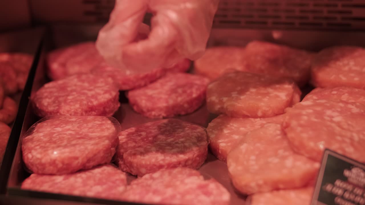 Butcher placing raw meat patties into plastic container at meat counter