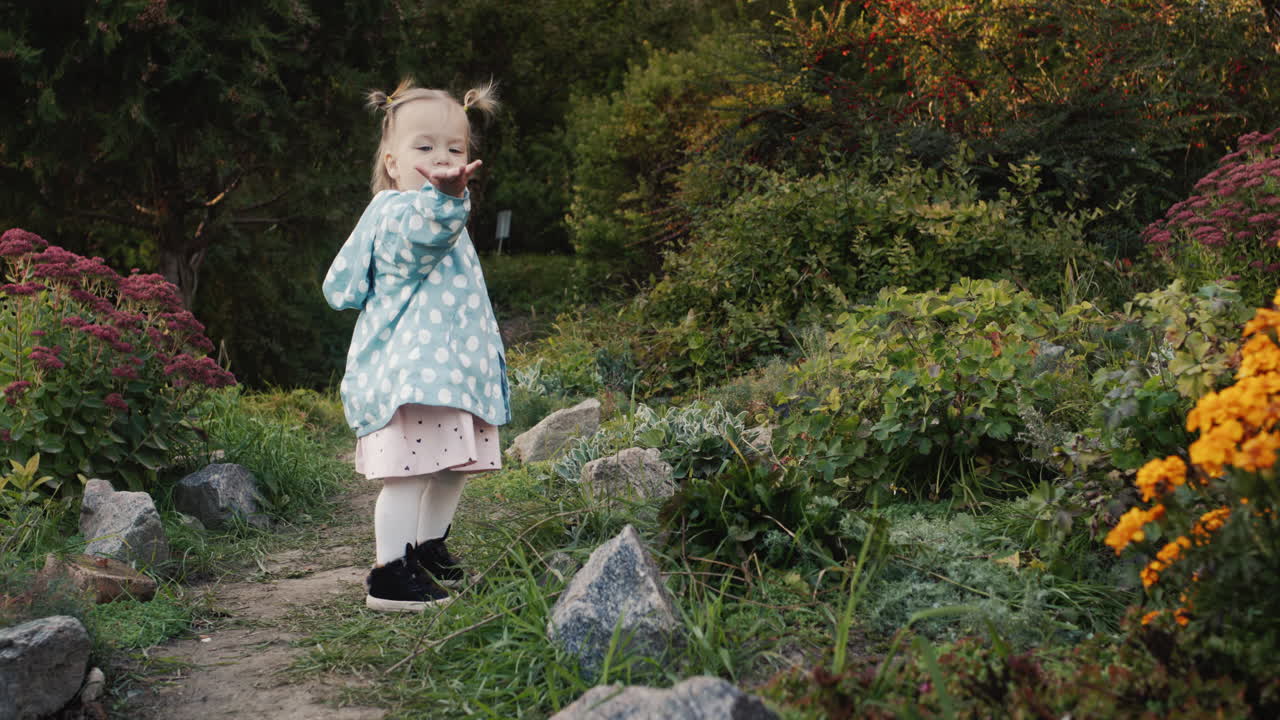 A little girl shows an air kiss and walks along a path in the park. Autumn Walk