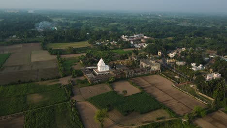 aerial drone shot of a pristine white temple, standing tall amidst green landscapes under a clear sky.