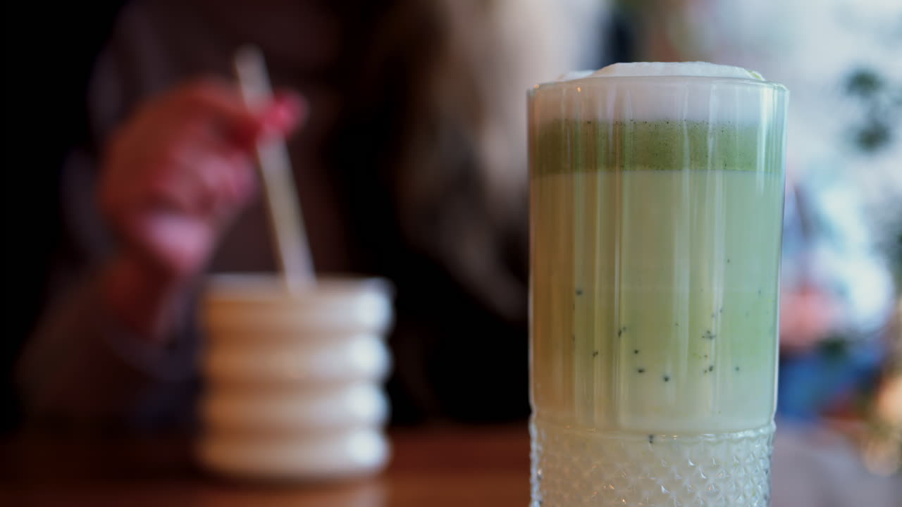 Close up of a matcha latte with a woman drinking at a table at a cafe on the background