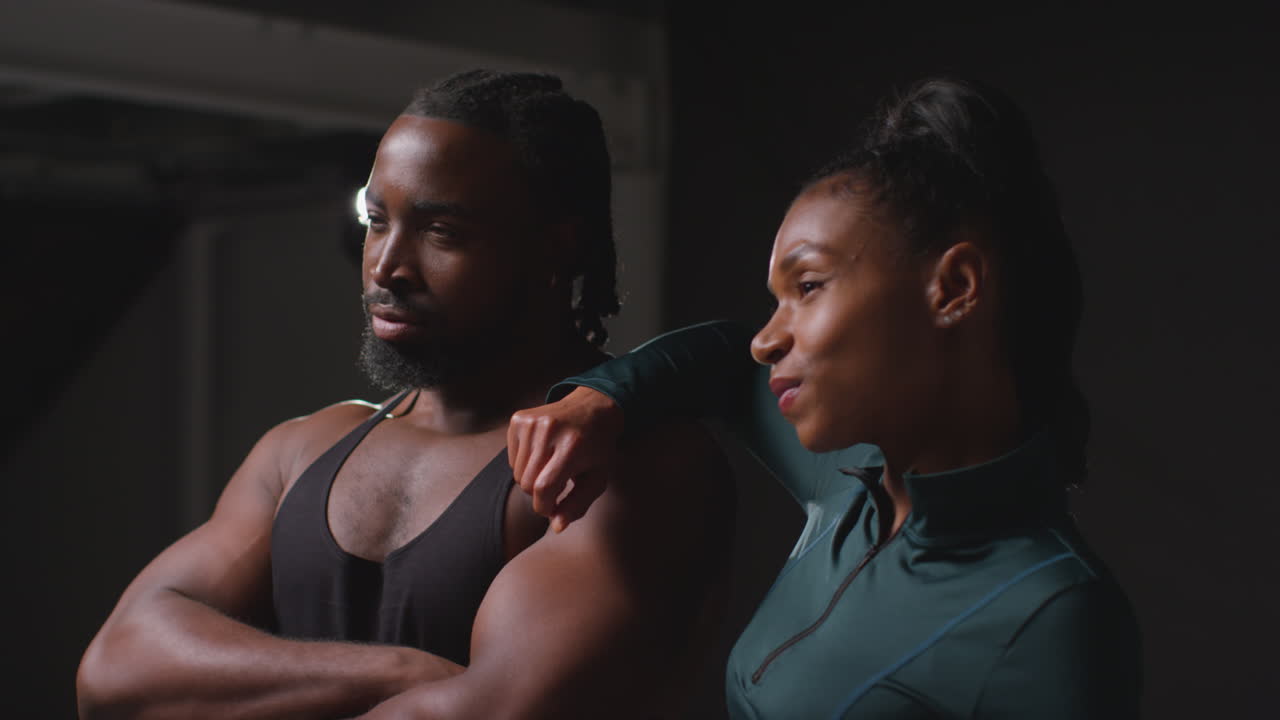 студийный портрет улыбающейся спортивной пары или друзей в фитнес-одежде, снятый в тренажерном зале при низком освещении 3