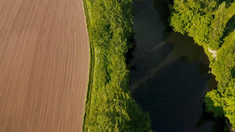 drone bird's eye view of freshly tilled field next to wide river lined with trees