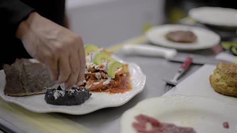 chef sou-chef cook preparing a traditional mexican dish called chilaquiles adding smashed black beans at a local cafe diner restaurant in latin america