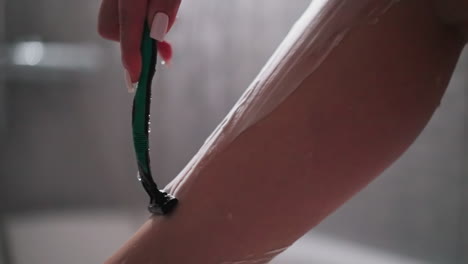 woman removes leg skin hair with razor in shower closeup. slim lady shaves body with sharp blade in bathroom. woman does beauty procedure at home