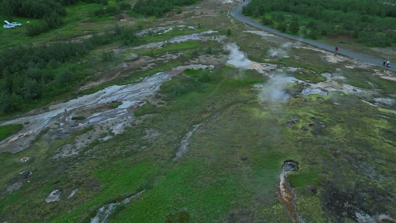 아이슬란드의 게이시르 (geysir) 에 있는 증기성 지열 지대의 드론 뷰, 거품이 있는 수영장, 울창한 초록색, 구름이 가득한 하늘 아래의 경로.