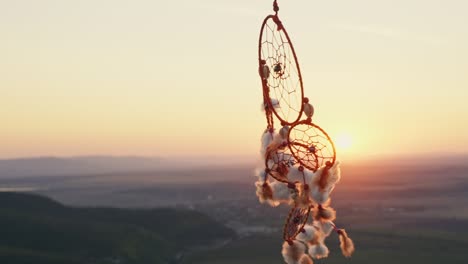 cazador de sueños con plumas naranjas gira en las montañas, balanceándose con el viento ligero movimiento lento de nuevo el cielo azul al atardecer en verano. amuleto estilo boho, estilo indio. disco brillante del sol, rayos de sol