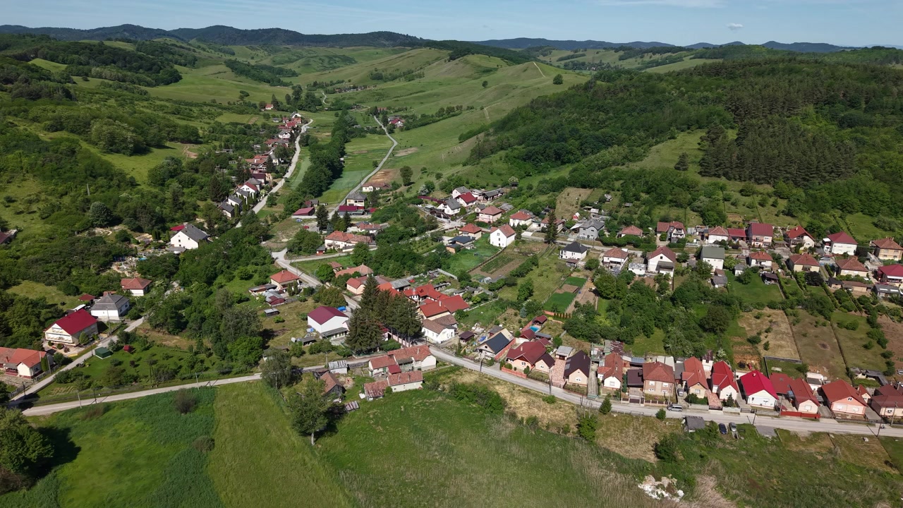 Letecký záběr dronem zachycuje malou vesnici ležící v bujném zeleném údolí obklopeném zvlněnými kopci.