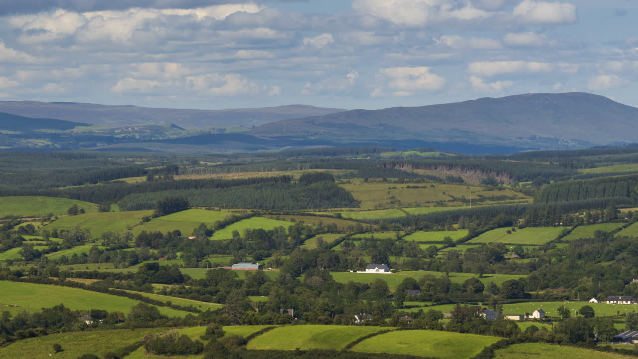 Time lapse of rural agriculture landscape with fields and farmhouses with hills in the distance on a sunny summer day in Ireland