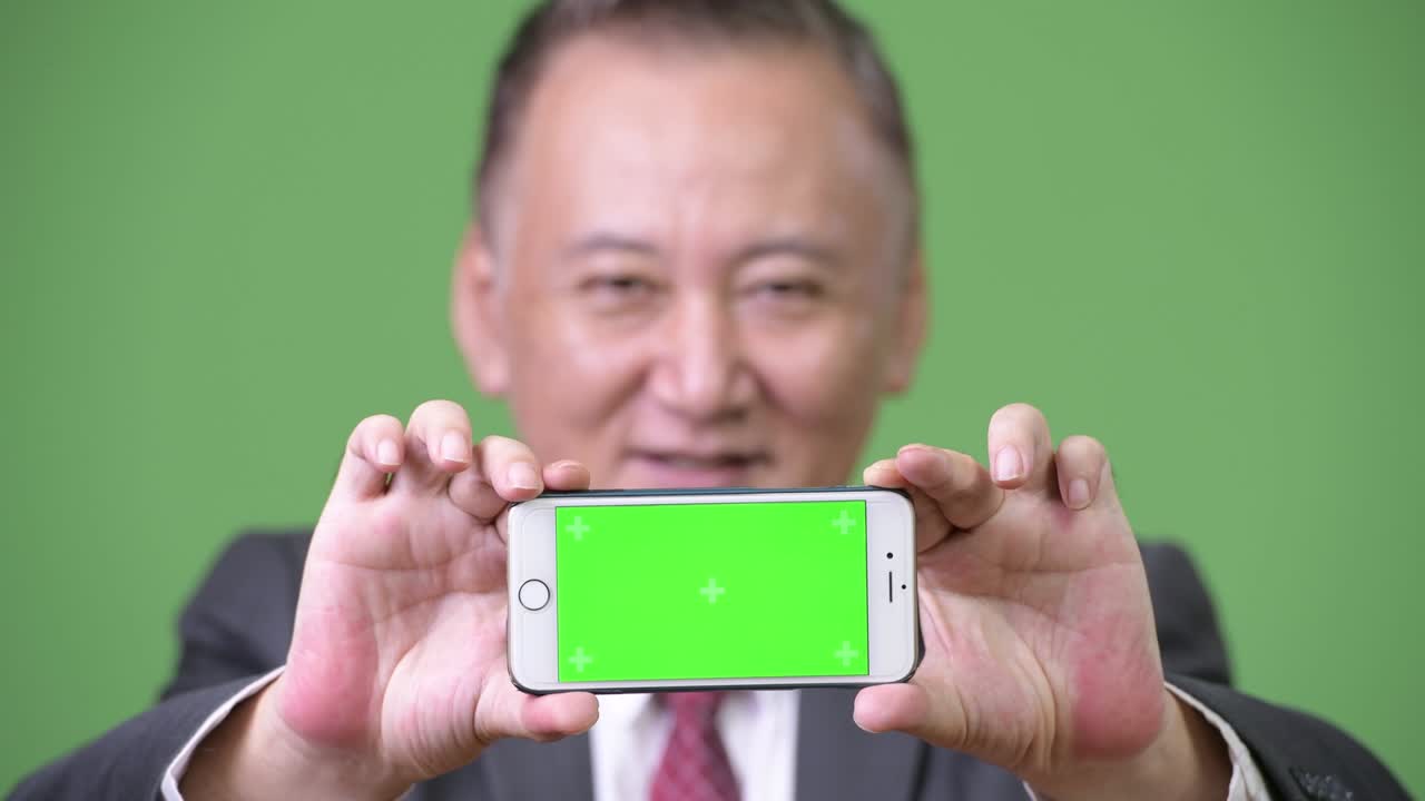 성숙 한 일본인 사업가 가 카메라 에 전화 를 보여주고 있다