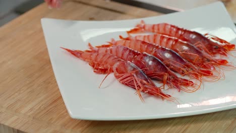 hand serves red shrimp on a plate on a wooden table