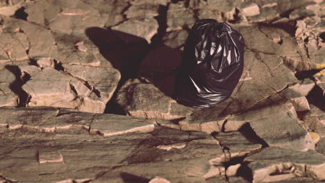 black trash bag lay on a rocky beach