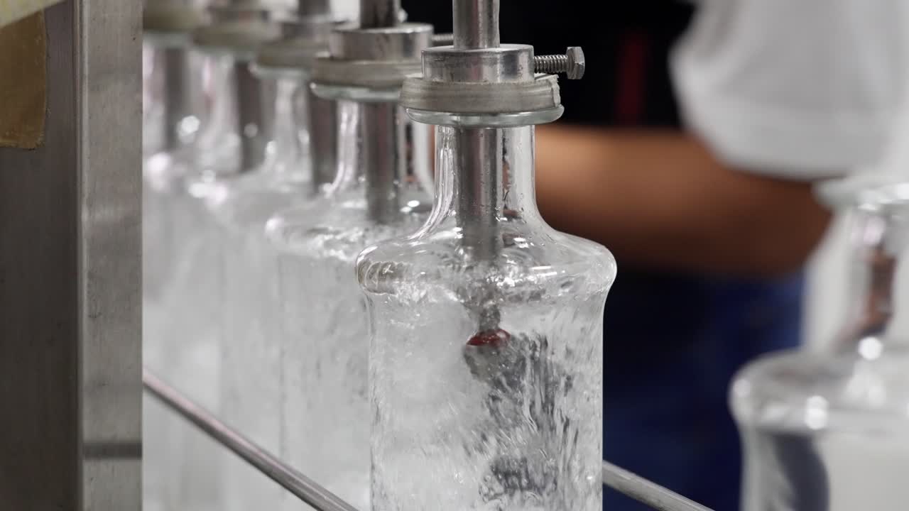 Industrial close-up of clear glass bottles filled with mezcal on a factory production line