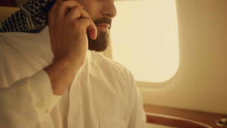 arabian businessman talking phone on private jet. closeup hand picking cellphone