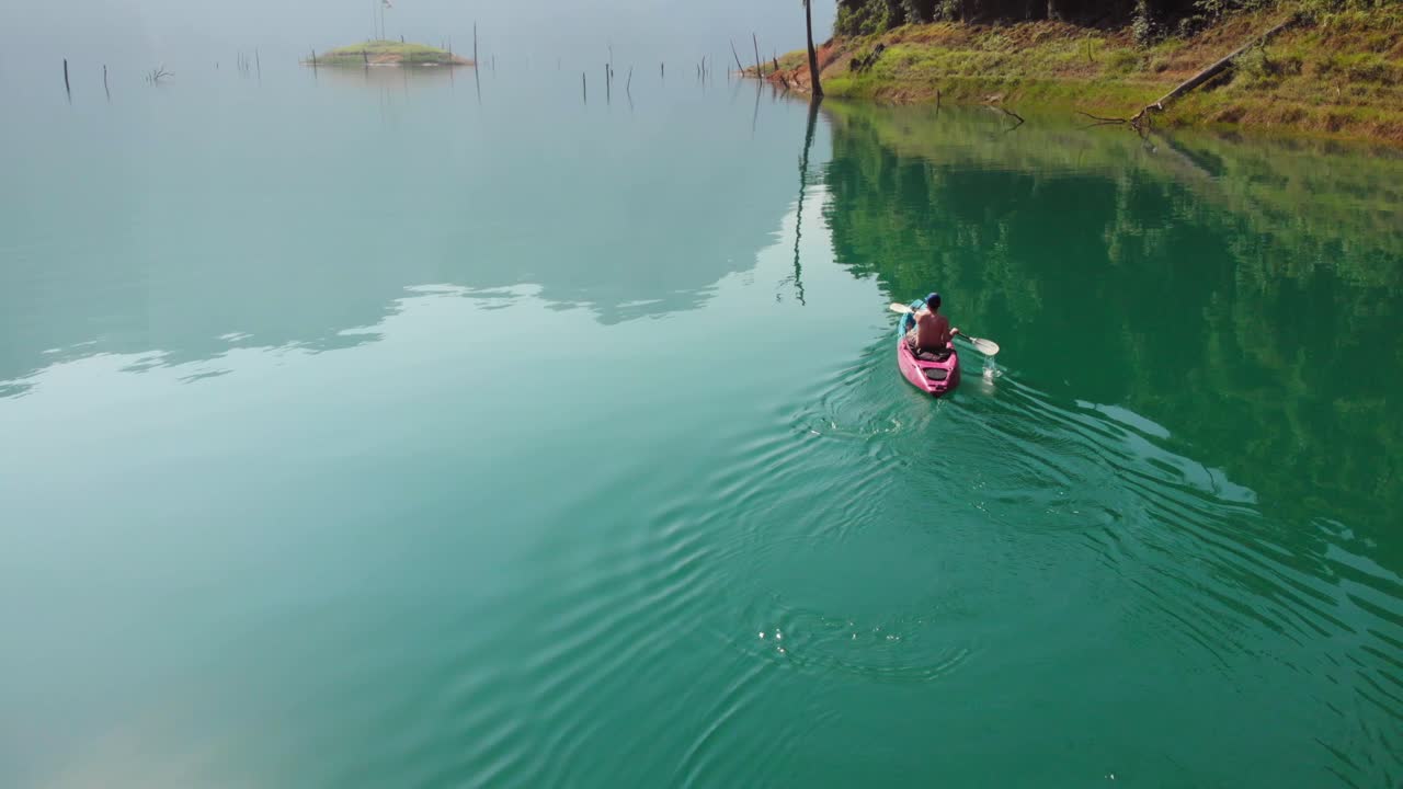 мужчина катается на каяке по безмятежному озеру cheow lan в национальном парке khao sok в яркий солнечный день в таиланде