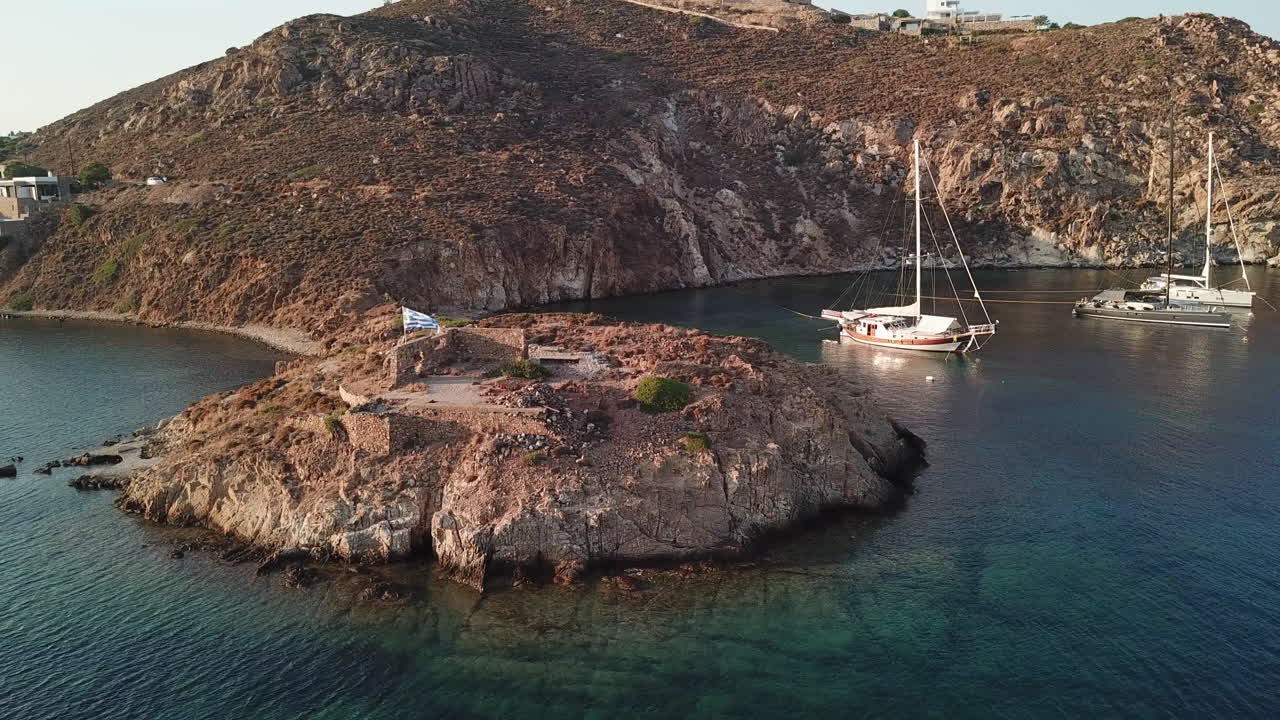 Greece,Patmos Island,Drone Footage, entrance of Grikos Bay, ruins of an old house and a big Greek flag. Boats stern to, beautiful colors of the Aegean sea. Picturesque island with beautiful landscapes