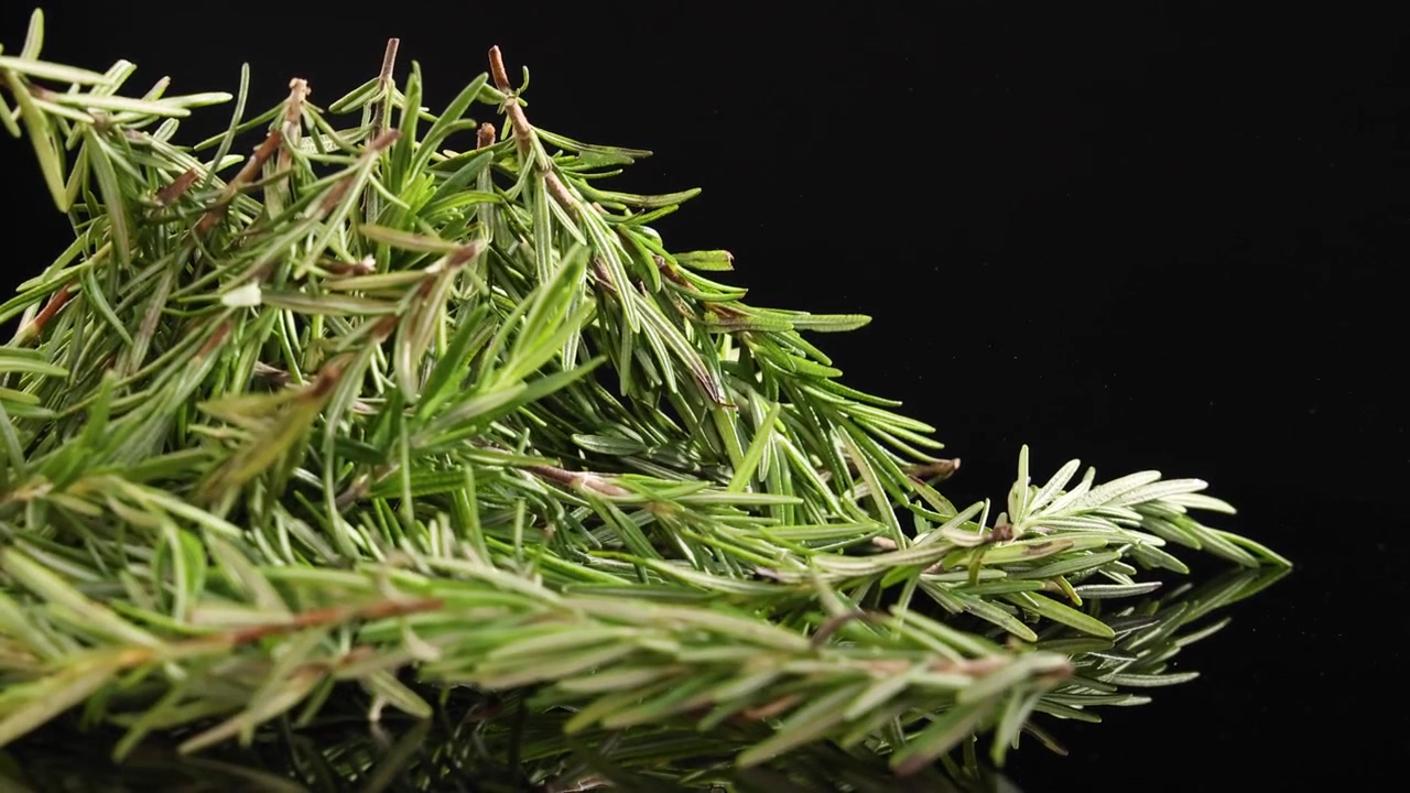 Rosemary sprigs gently drop onto a surface, captured in slow motion against a dark backdrop