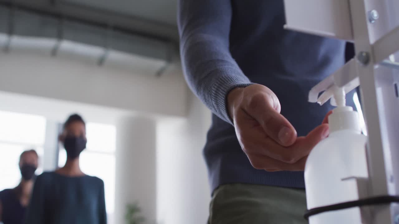 Work colleagues wearing face masks using sanitizer to disinfect hands as they enter the workplace