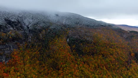 approaching a high mountain with a top covered with snow. bright colorful forest growing on the slopes of the rock. aerial view.