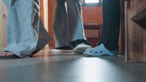 low angle leg view of person entering wooden room wearing light blue slippers and black pants, soft daylight illuminating warm wooden interior with furniture in background