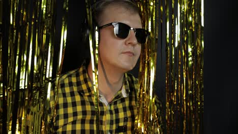 portrait of caucasian man dancing on black background. gold shining foil strips. party, music, disco