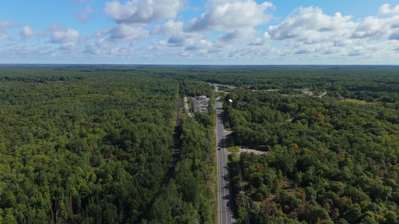 Drone moving forward above road dividing dense Muskoka forest
