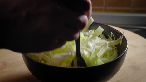 person is mixing sliced cabbage in a small bowl using two forks