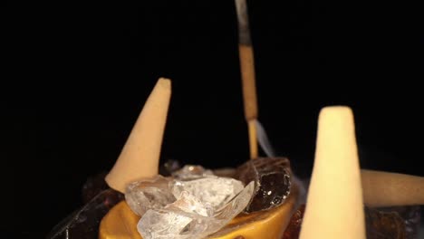 pushing past several unlit incense cones in a decorative rock garden, towards a lit stick with smoke billowing out the bottom