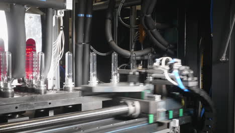 a closeup look at the piece of robotized equipment producing plastic bottles from transparent pet plastic preforms