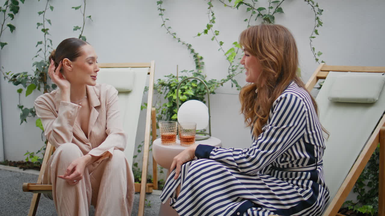 Girls friends chatting patio surrounded by greenery closeup. Smiling girlfriends