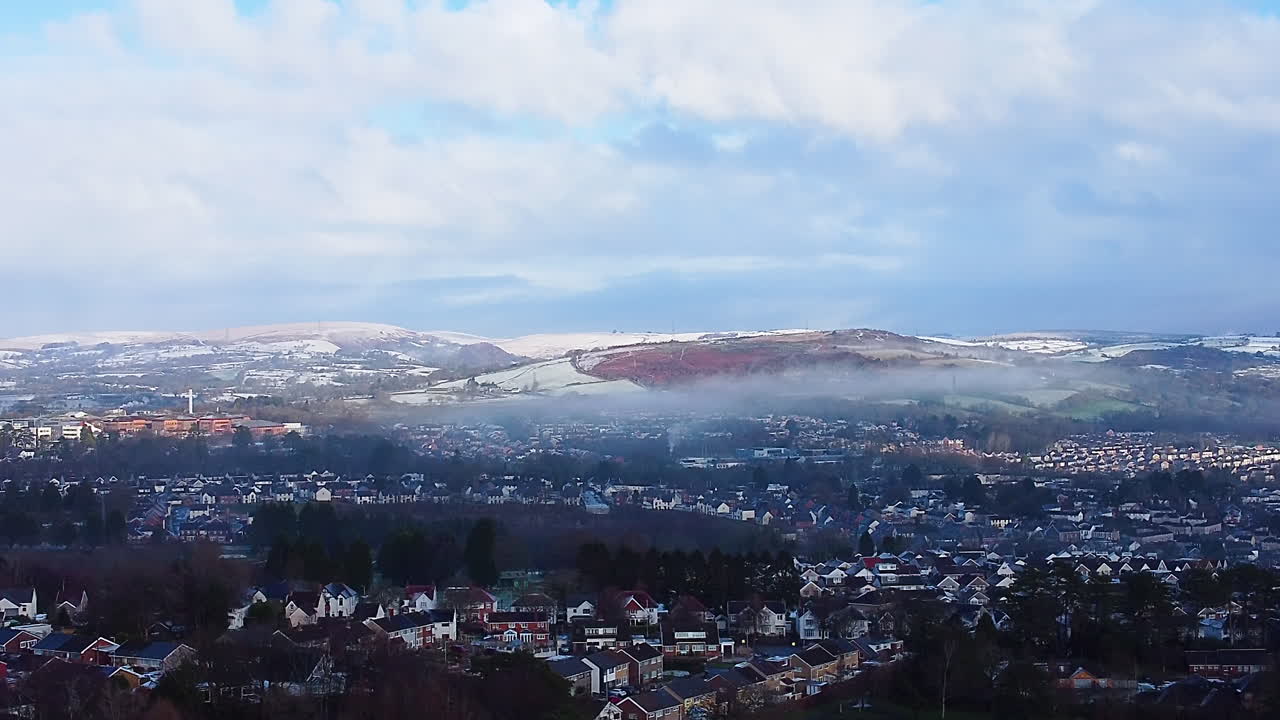 Vinterligt luftfoto over Swansea, Wales, med omvendte lavthængende skyer omkring forstadshuse med spredte træer og sneklædte bakker. Indfanger den fredelige natur i et boligområde.