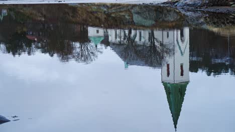 ljungs kyrka church reflected over still lake waters in ljungskile, bohuslan, sweden. tilt-down shot