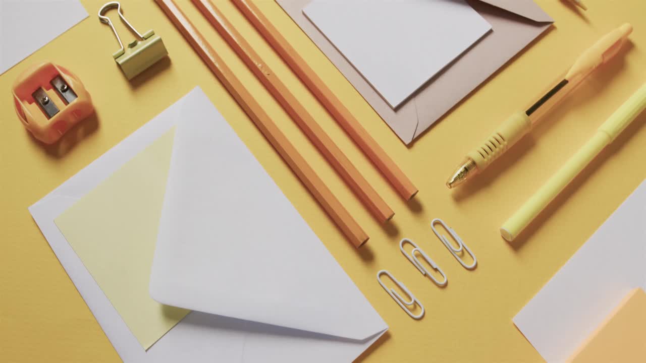 Close up of pens, pencils and stationery arranged on yellow background, in slow motion