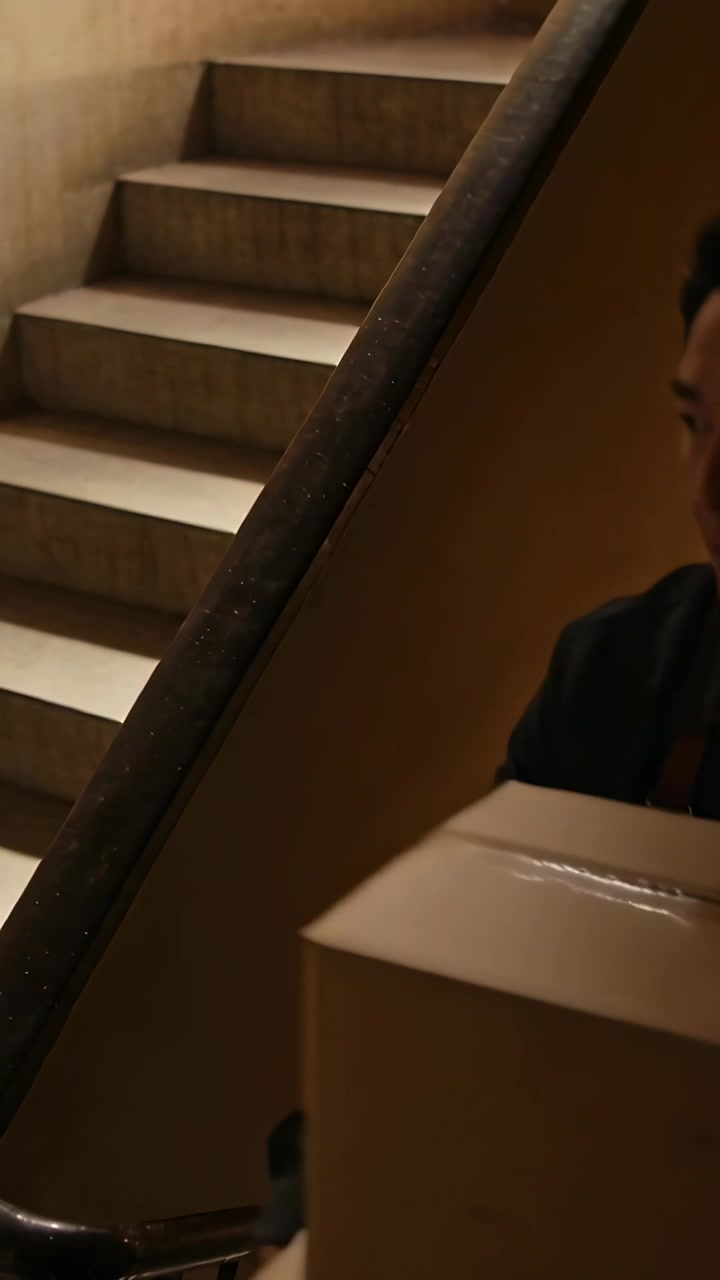 Vertical video: Entering man in dark jacket carrying boxes in stairwell by handrail, copy space