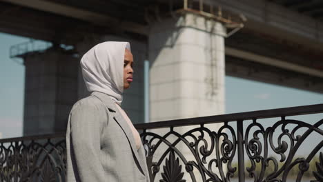 sad arabian woman stands by fence on town embankment