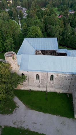 vertical drone footage captures the historic padise monastery surrounded by green fields and forests showcasing its medieval stone walls and timeless architecture in the peaceful estonian countryside