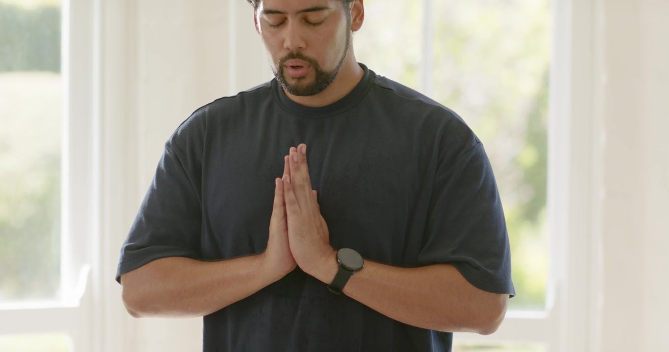 African American midadult man holding palms, breathing, closing eyes by window with smartwatch