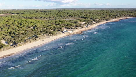 Trenc-Beach-in-Mallorca-Spain-with-a-concrete-building-foundation-pounded-by-waves,-Aerial-approach-shot