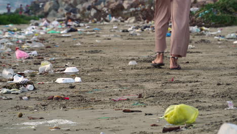 pies de mujer caminando en una playa sucia contaminada ambientalmente con basura