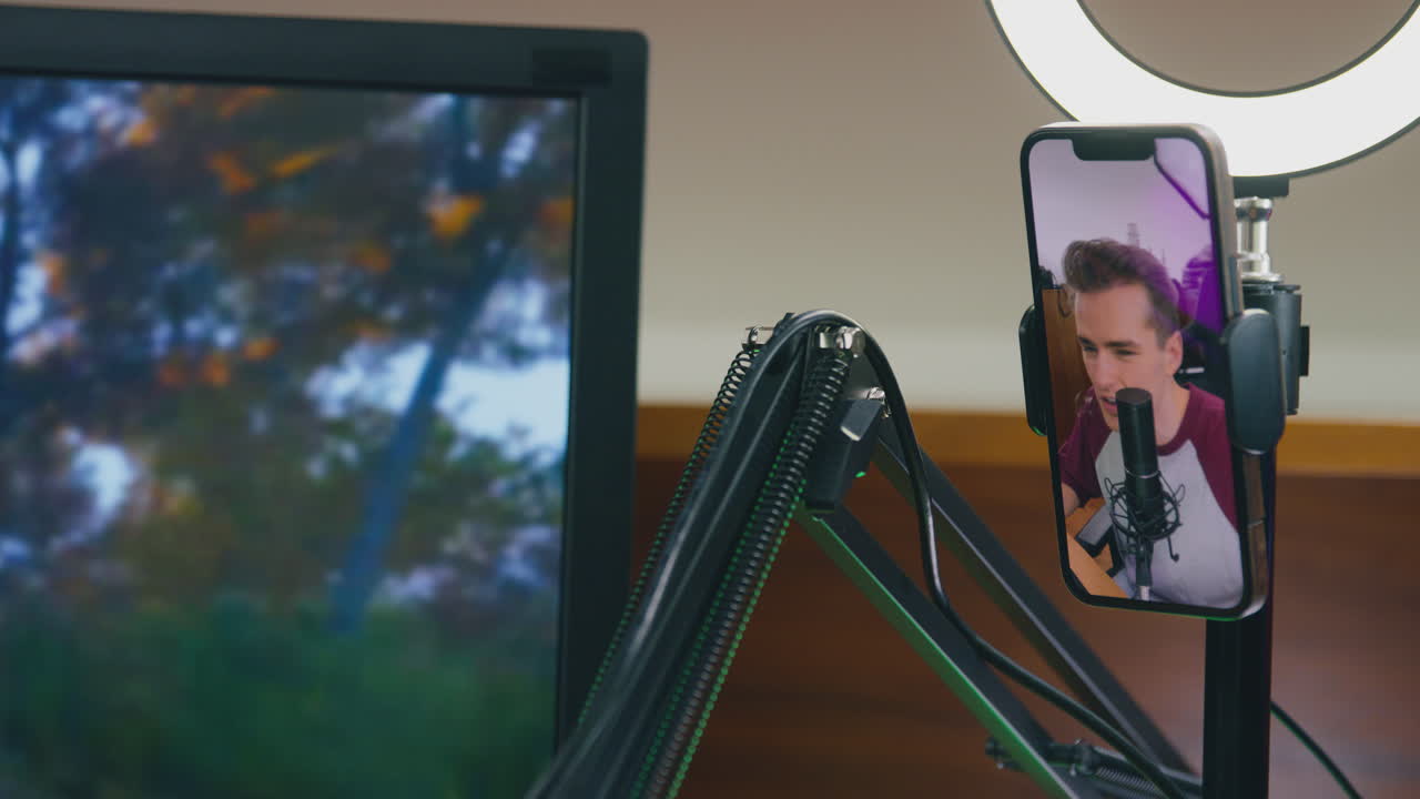 hombre jugando en casa sentado en el escritorio transmisión en vivo juego de disparos desde el teléfono móvil