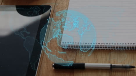 animation of spinning globe over close up of office equipment on wooden table