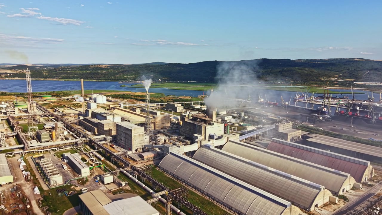 View of a large industrial area near a lake with smoke coming from factories and ships docked at the port