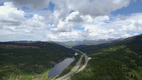 Toma-Aérea-De-Un-Dron-De-La-Carretera-Interestatal-70-I-70-Que-Atraviesa-El-Paisaje-De-Las-Montañas-Rocosas-Del-Bosque-Alpino-Durante-El-Día-De-Verano