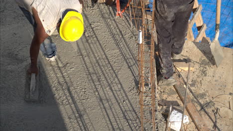 una toma en cámara lenta de un trabajador de la construcción latino mexicano con un casco aplanando el hormigón fresco usando una paleta de madera en una tarde soleada