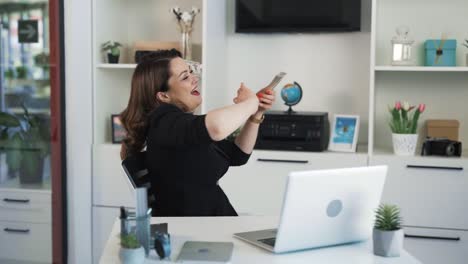 the happy female boss is sitting in her office and rejoicing over the earned money, scattering banknotes in front of her