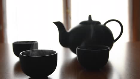 minimal background of a green japanese tea set with steam coming out of the cups, on a wooden table, with a window in the back