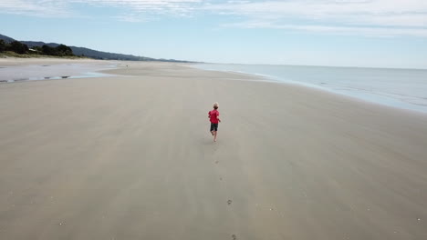 aerial following shot of a boy running along a beach